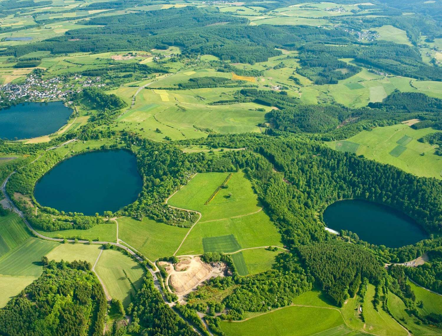 Luftaufnahme auf die Maare. Im Hintergrund am letzten Maar ist eine Ortschaft zu erkennen.