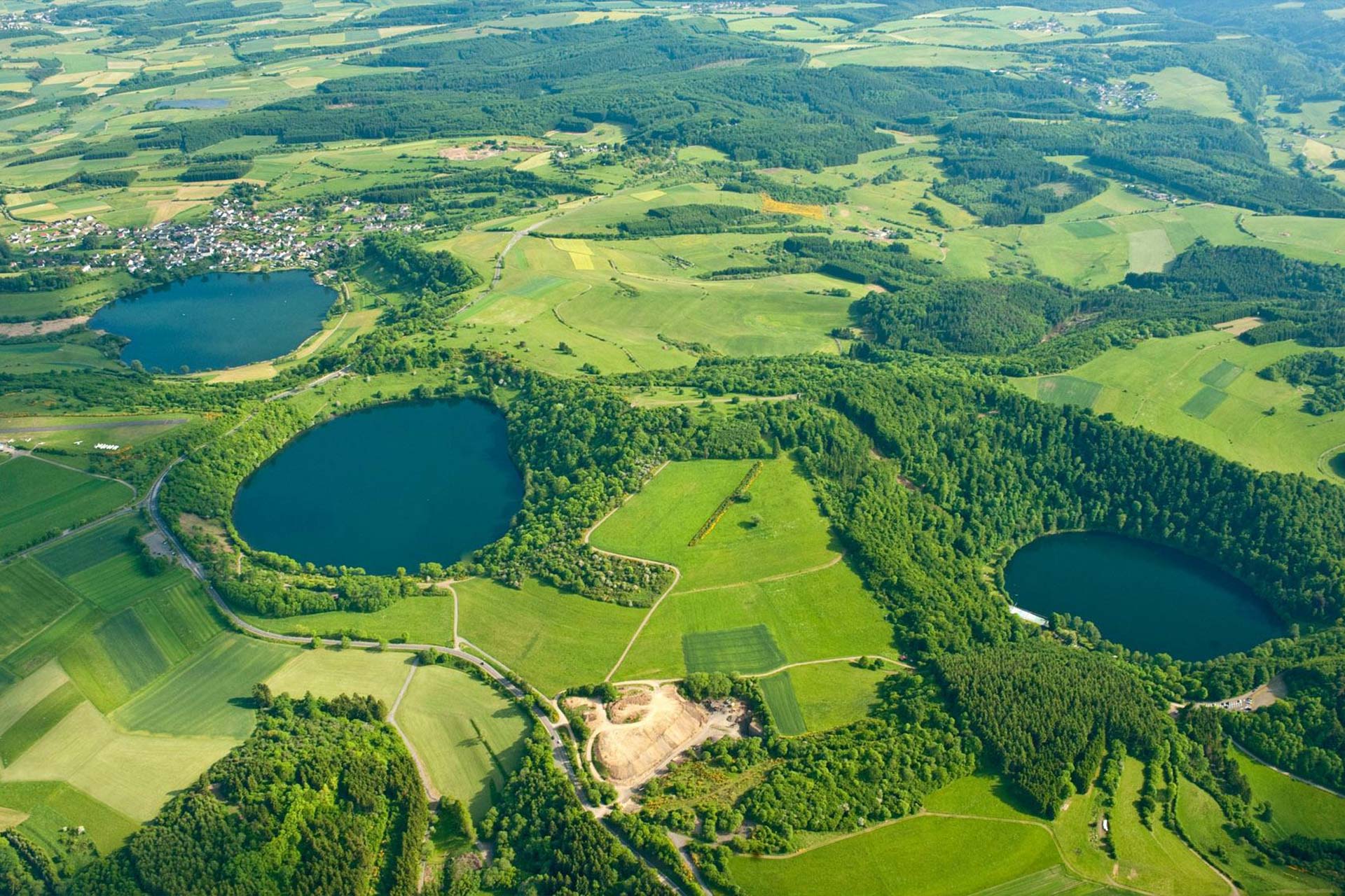 Luftaufnahme auf die Maare. Im Hintergrund am letzten Maar ist eine Ortschaft zu erkennen.