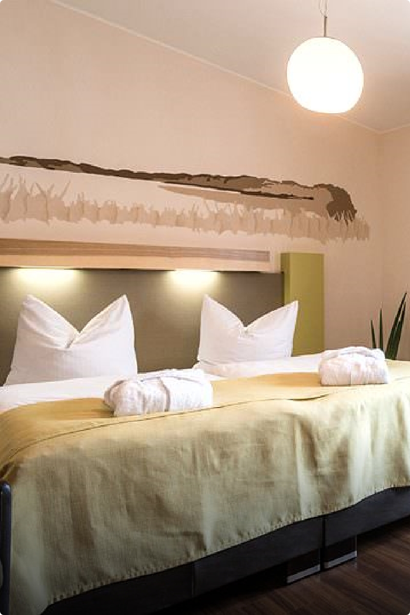 Eifelart Wohlfühl-Doppelzimmer mit Doppelbett im Focus, mit weißen Matratzen- und Kissenüberzug sowie einer grünen Überdecke.
