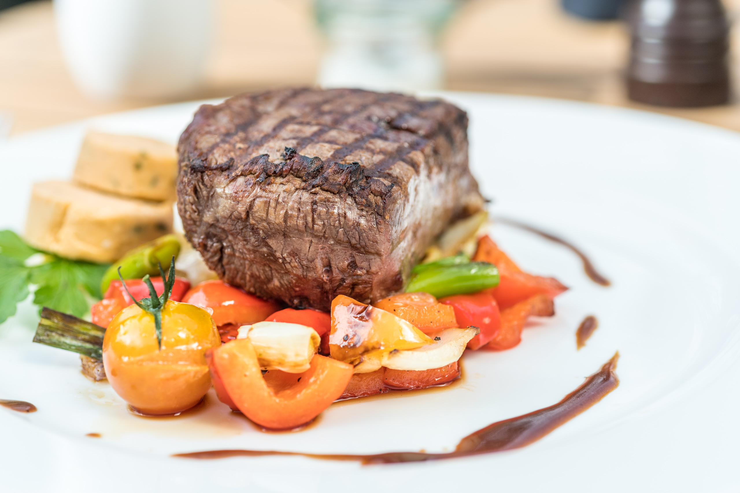 Steak auf Gemüse der Saison, garniert auf einem weißen Teller mit Soßenspiegel